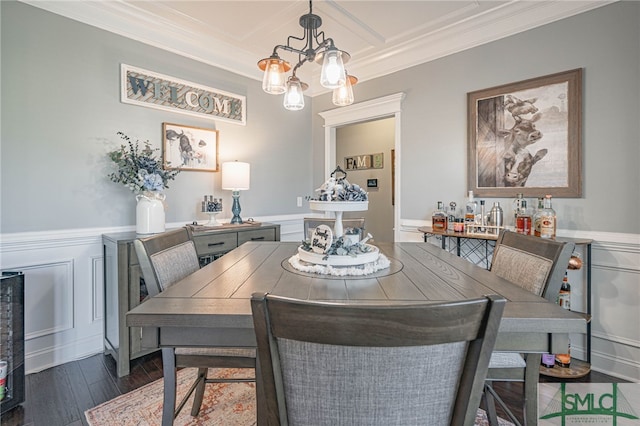 dining space with a wainscoted wall, dark wood-style floors, ornamental molding, a decorative wall, and a notable chandelier