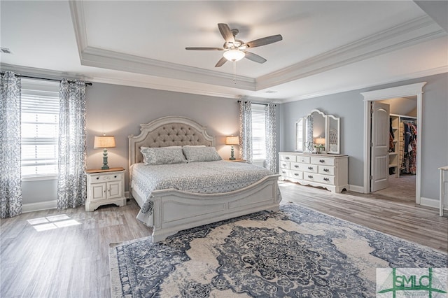 bedroom featuring ceiling fan, a raised ceiling, light wood-type flooring, baseboards, and ornamental molding