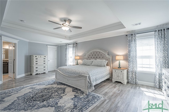 bedroom with visible vents, light wood-style floors, multiple windows, and a tray ceiling