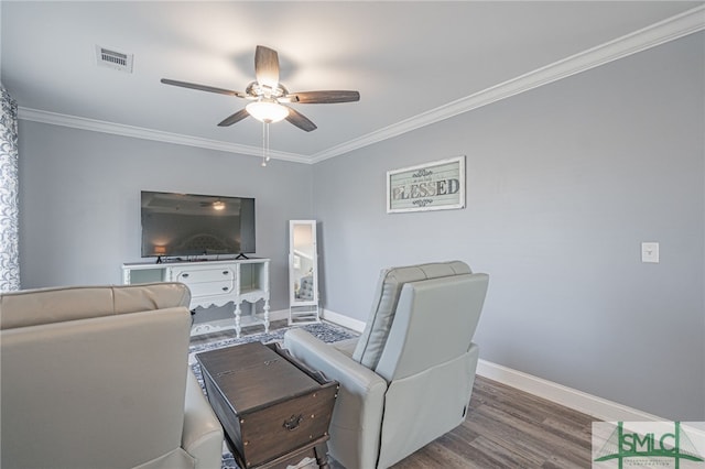 living area featuring wood finished floors, ornamental molding, baseboards, visible vents, and a ceiling fan