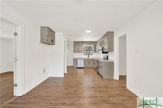 kitchen featuring a sink, light wood-type flooring, light countertops, gray cabinetry, and appliances with stainless steel finishes