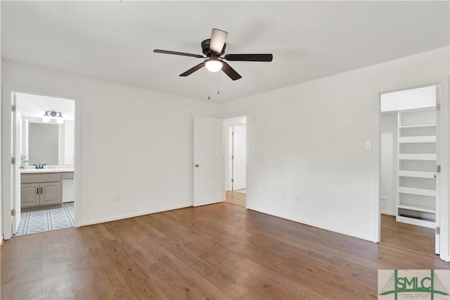 unfurnished bedroom with a walk in closet, baseboards, wood finished floors, and ensuite bath
