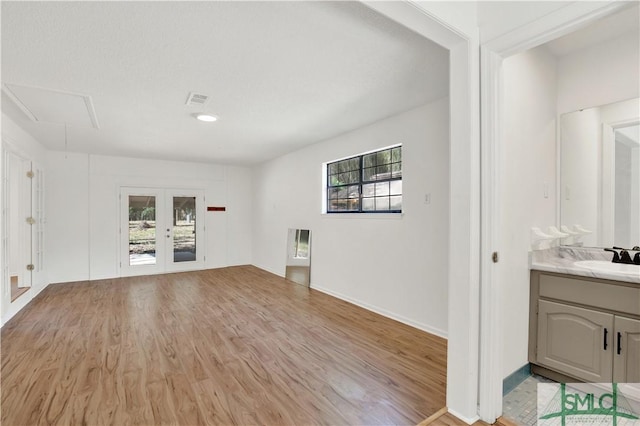 interior space with a sink, light wood-style floors, visible vents, attic access, and french doors