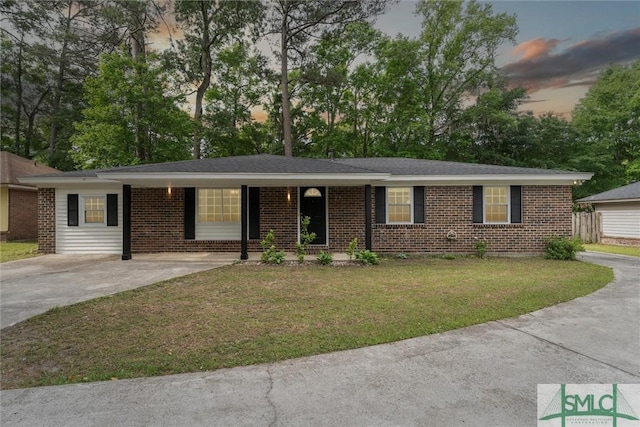 ranch-style home featuring driveway, covered porch, a yard, and brick siding