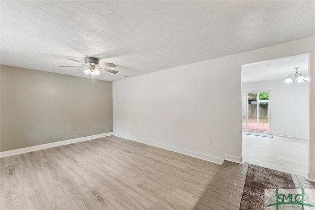 spare room featuring a textured ceiling, baseboards, wood finished floors, and ceiling fan with notable chandelier