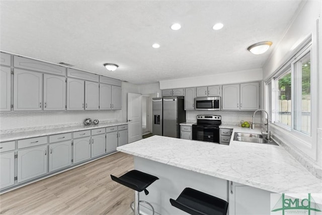 kitchen with appliances with stainless steel finishes, a peninsula, gray cabinets, and a sink