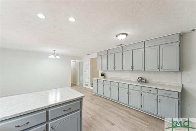 kitchen featuring a textured ceiling, light wood-style flooring, gray cabinetry, light countertops, and an inviting chandelier