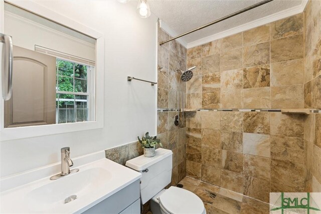 bathroom featuring a textured ceiling, a tile shower, toilet, ornamental molding, and vanity