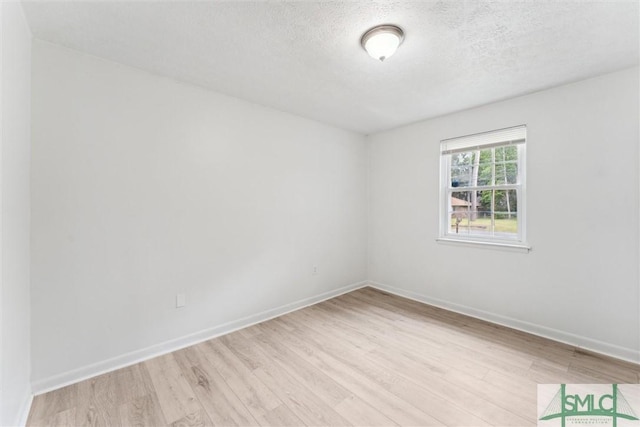 spare room featuring a textured ceiling, light wood-style flooring, and baseboards