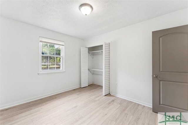 unfurnished bedroom featuring a textured ceiling, light wood-style floors, baseboards, and a closet