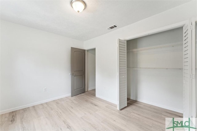 unfurnished bedroom with a closet, visible vents, wood finished floors, and baseboards