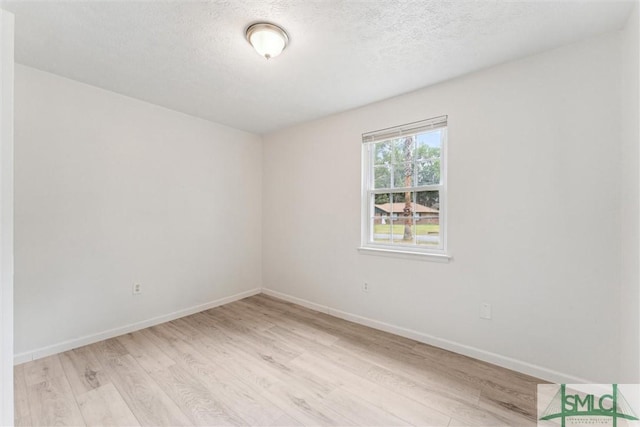 empty room with a textured ceiling, light wood-style flooring, and baseboards