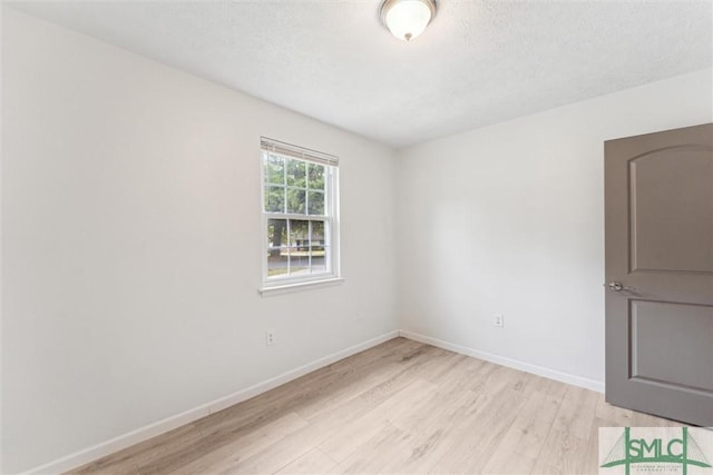 unfurnished room with a textured ceiling, light wood-type flooring, and baseboards