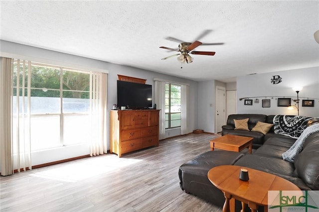 living area featuring baseboards, a textured ceiling, ceiling fan, and light wood-style flooring