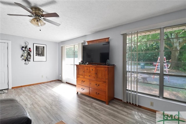 living area featuring baseboards, ceiling fan, and a textured ceiling