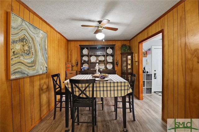 dining room featuring crown molding, a ceiling fan, wood finished floors, and wooden walls