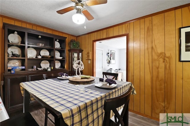 dining room featuring a ceiling fan, wood walls, and wood finished floors