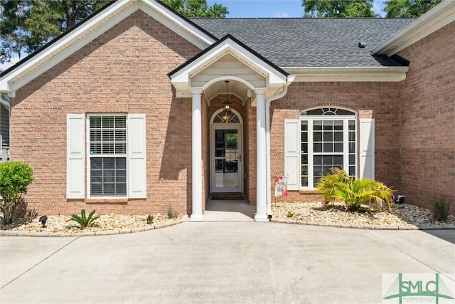 doorway to property with brick siding and roof with shingles