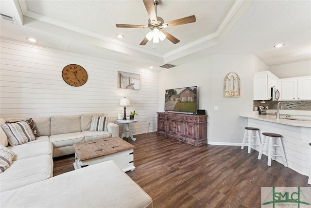 living room featuring visible vents, ceiling fan, a tray ceiling, dark wood-style floors, and ornamental molding