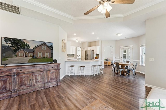 interior space with arched walkways, dark wood-style floors, visible vents, a ceiling fan, and crown molding