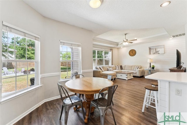 dining area with visible vents, a tray ceiling, baseboards, dark wood finished floors, and a ceiling fan