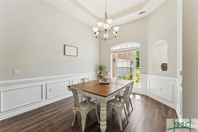 dining area with visible vents, a tray ceiling, dark wood-style flooring, a decorative wall, and a notable chandelier
