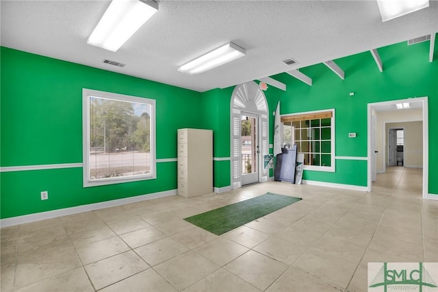 tiled spare room with a textured ceiling, visible vents, plenty of natural light, and baseboards