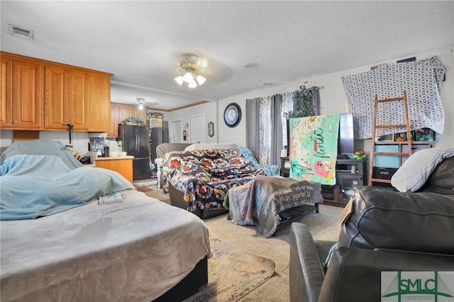 bedroom with light colored carpet, visible vents, freestanding refrigerator, and a textured ceiling
