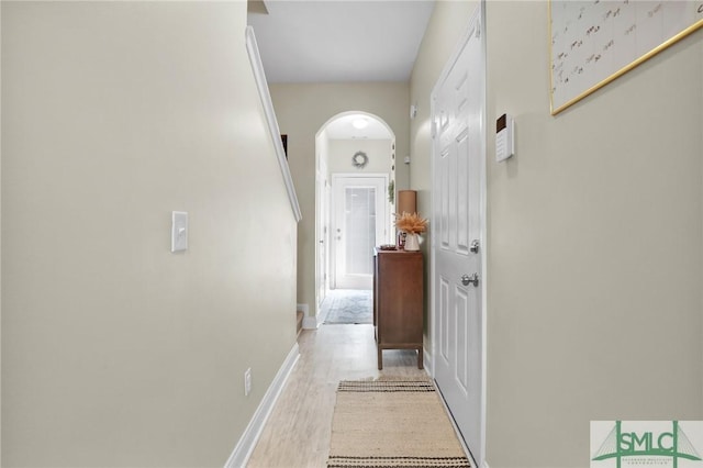 hall with light wood-type flooring, arched walkways, and baseboards