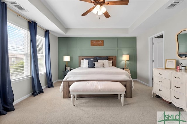 bedroom featuring visible vents, light colored carpet, and a tray ceiling