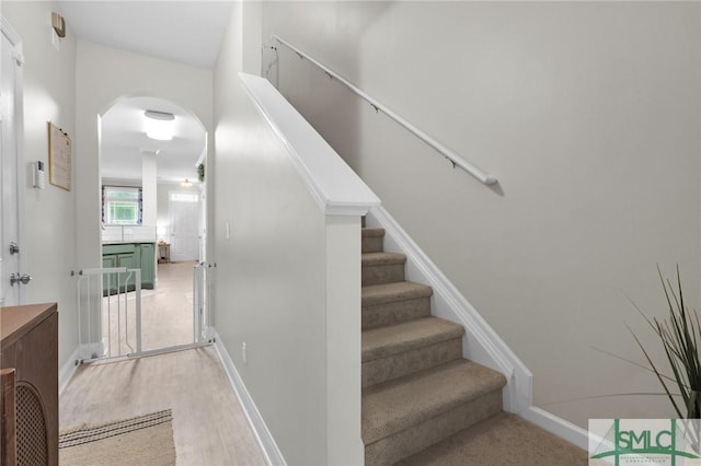 stairway featuring wood finished floors, baseboards, and arched walkways