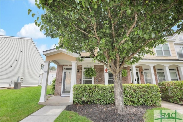 townhome / multi-family property with a porch, a front yard, and brick siding