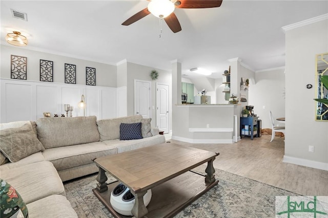 living room with crown molding, visible vents, ceiling fan, baseboards, and light wood-type flooring