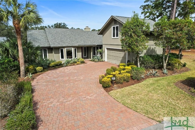 view of front of home with decorative driveway, an attached garage, a chimney, and a shingled roof