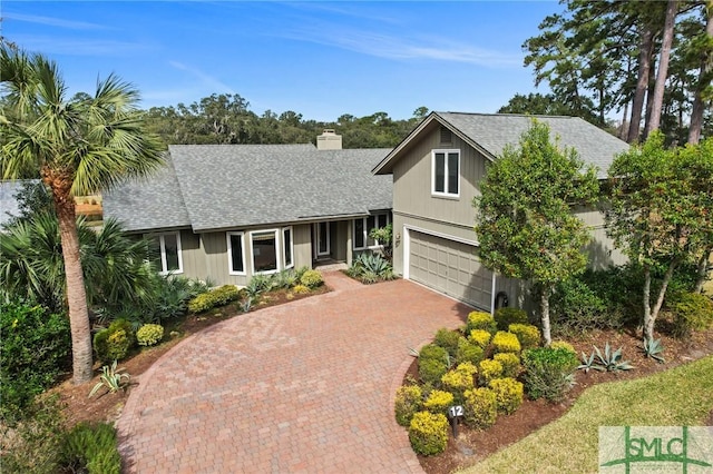 view of front of home with roof with shingles, an attached garage, a chimney, and decorative driveway