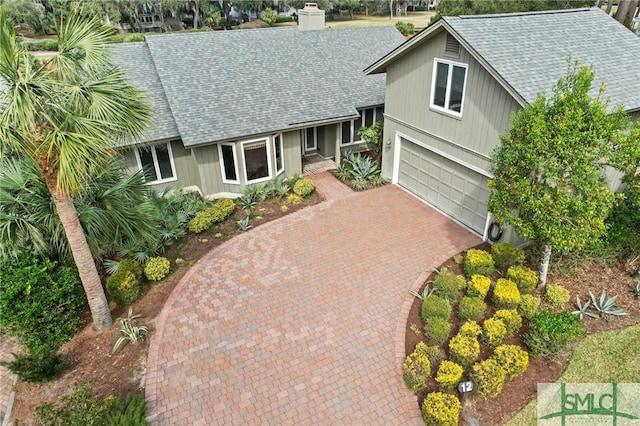view of front of home with decorative driveway, an attached garage, a shingled roof, and a chimney