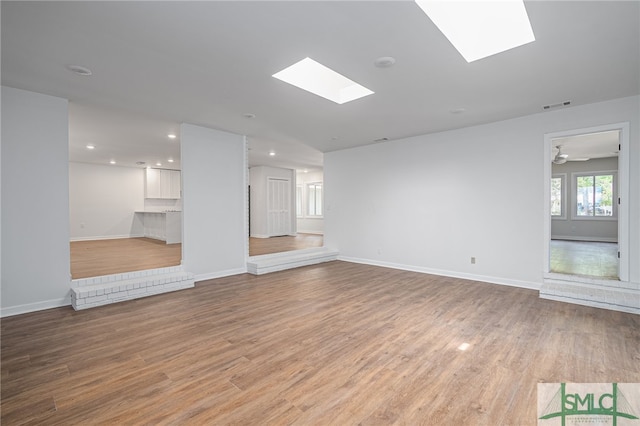 unfurnished living room featuring baseboards, light wood-style flooring, visible vents, and a skylight
