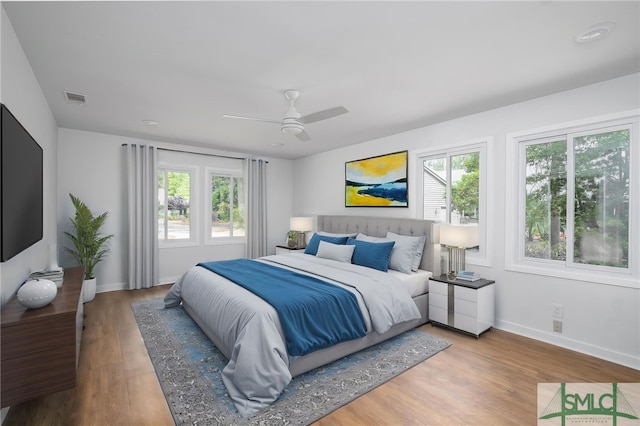 bedroom with visible vents, baseboards, wood finished floors, and multiple windows