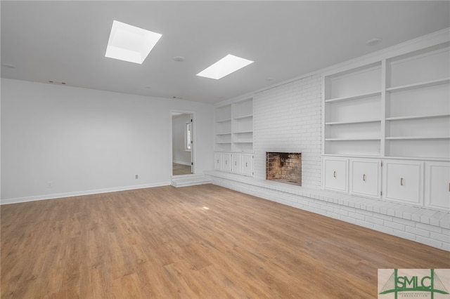 unfurnished living room with a skylight, built in features, a fireplace, light wood-type flooring, and baseboards