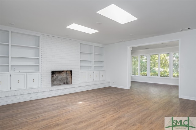 unfurnished living room featuring a brick fireplace, wood finished floors, baseboards, built in shelves, and a skylight