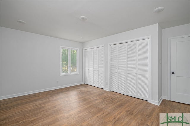 unfurnished bedroom featuring baseboards, multiple closets, and wood finished floors