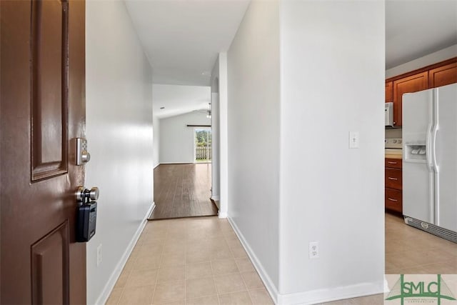 hallway with light tile patterned floors, baseboards, and vaulted ceiling