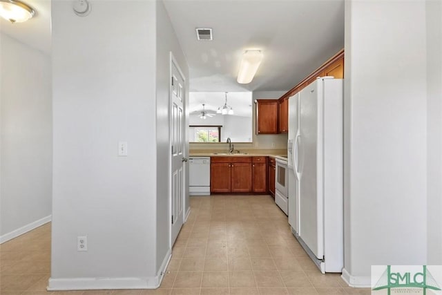 kitchen featuring visible vents, brown cabinetry, white appliances, a sink, and light tile patterned floors