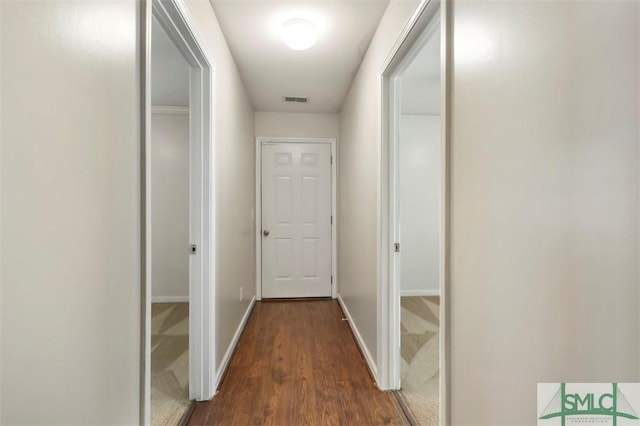 hall featuring baseboards, dark wood-type flooring, dark colored carpet, and visible vents