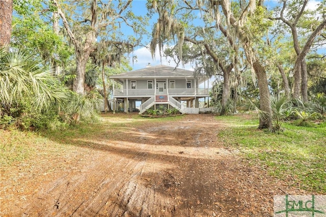 back of property featuring stairs, dirt driveway, and a porch