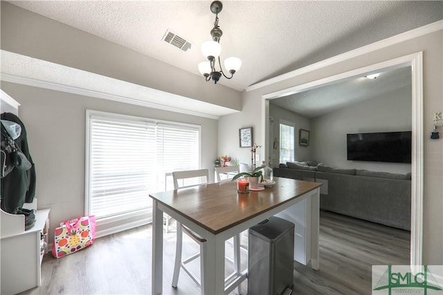 dining space with a textured ceiling, ornamental molding, wood finished floors, and visible vents