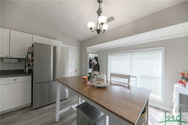 dining space featuring lofted ceiling, light wood finished floors, a chandelier, and visible vents