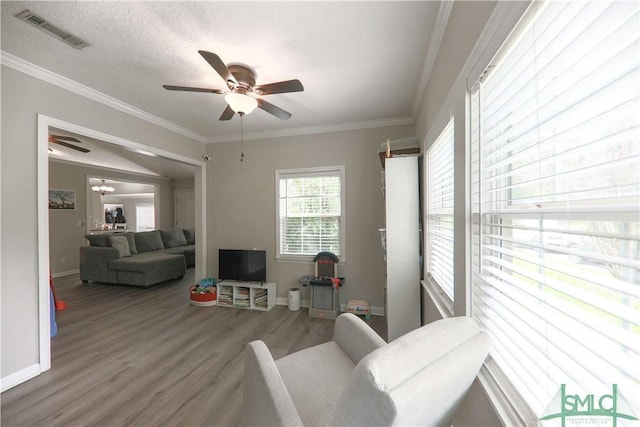 living room with a ceiling fan, visible vents, crown molding, wood finished floors, and baseboards