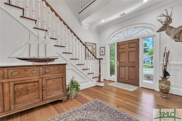 entrance foyer with visible vents, ornamental molding, light wood-style floors, and stairs