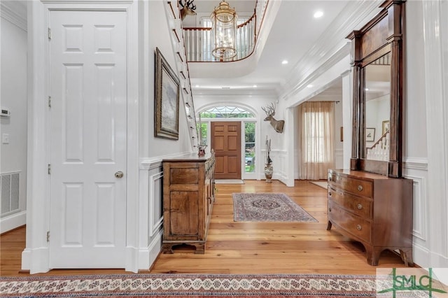 foyer entrance with crown molding, visible vents, a decorative wall, light wood-type flooring, and a notable chandelier